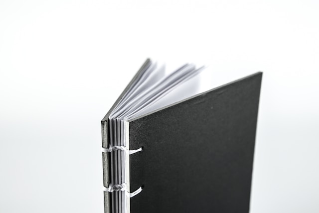 a black notebook bound by white string standing upright with its pages open